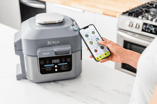 Ninja ON400DE Heißluftfritteuse auf Küchentisch mit geöffneter App auf Smartphone